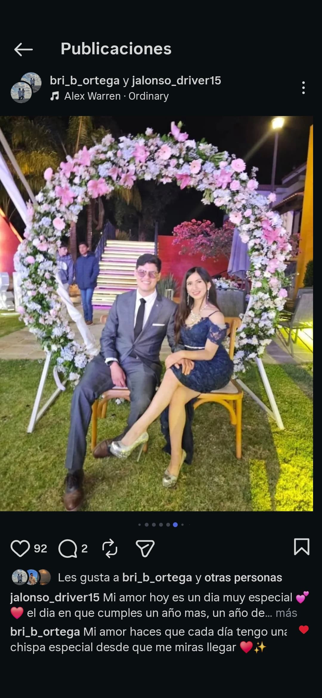 Pareja elegante posando bajo un arco circular de flores rosas y blancas en una fiesta.